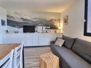 A modern living room with a grey sofa, wooden coffee table, and a TV on a white cabinet.