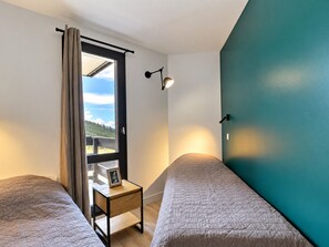 Un dormitorio con dos camas, una mesita de noche con un marco de fotos, una ventana con cortinas y una lámpara de pared.