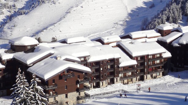 Uma pousada coberta de neve com vários andares, pistas de esqui e um teleférico.