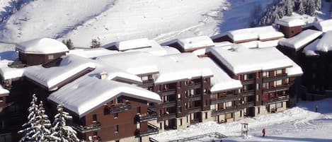 Un lodge cubierto de nieve con varios pisos, pistas de esquí y un telesilla.
