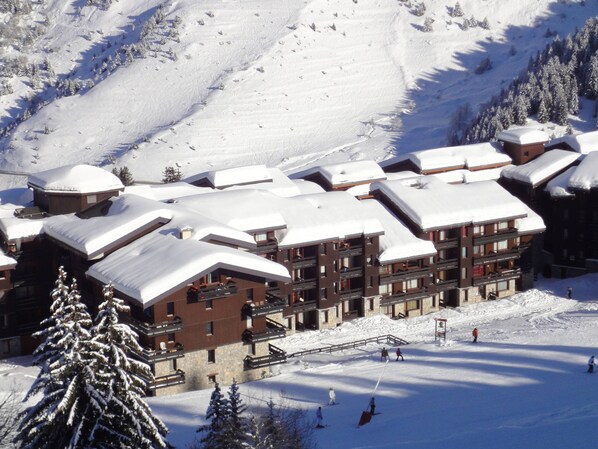 Un lodge cubierto de nieve con varios pisos, pistas de esquí y un telesilla.