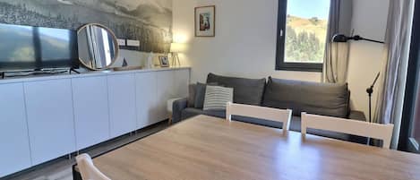 Un espacio moderno para vivir con una mesa de comedor, sillas blancas, un sofá y un amplio ventanal con cortinas.
