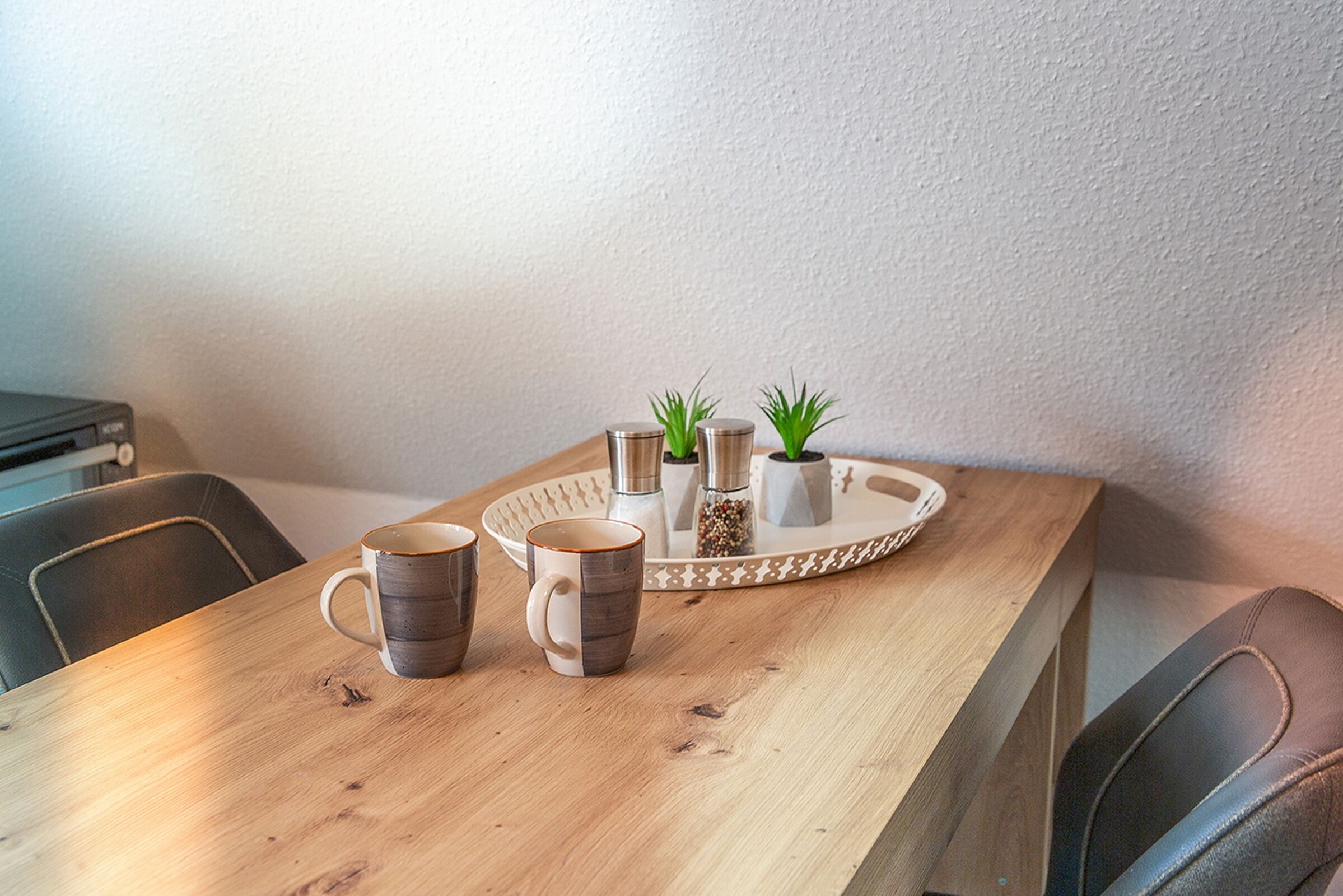 A wooden table with two mugs and a tray with salt, pepper, and a small plant.