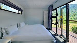 A large bed in a room with a view of a green landscape through a glass door.