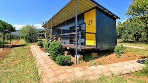 A modern building with a yellow and grey exterior, marked with the number 21, featuring a covered outdoor area and a stone pathway.
