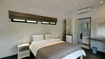 Quarto de hotel moderno com uma cama grande, mesas de cabeceira, escrivaninha, espelho e banheiro com pia e espelho.