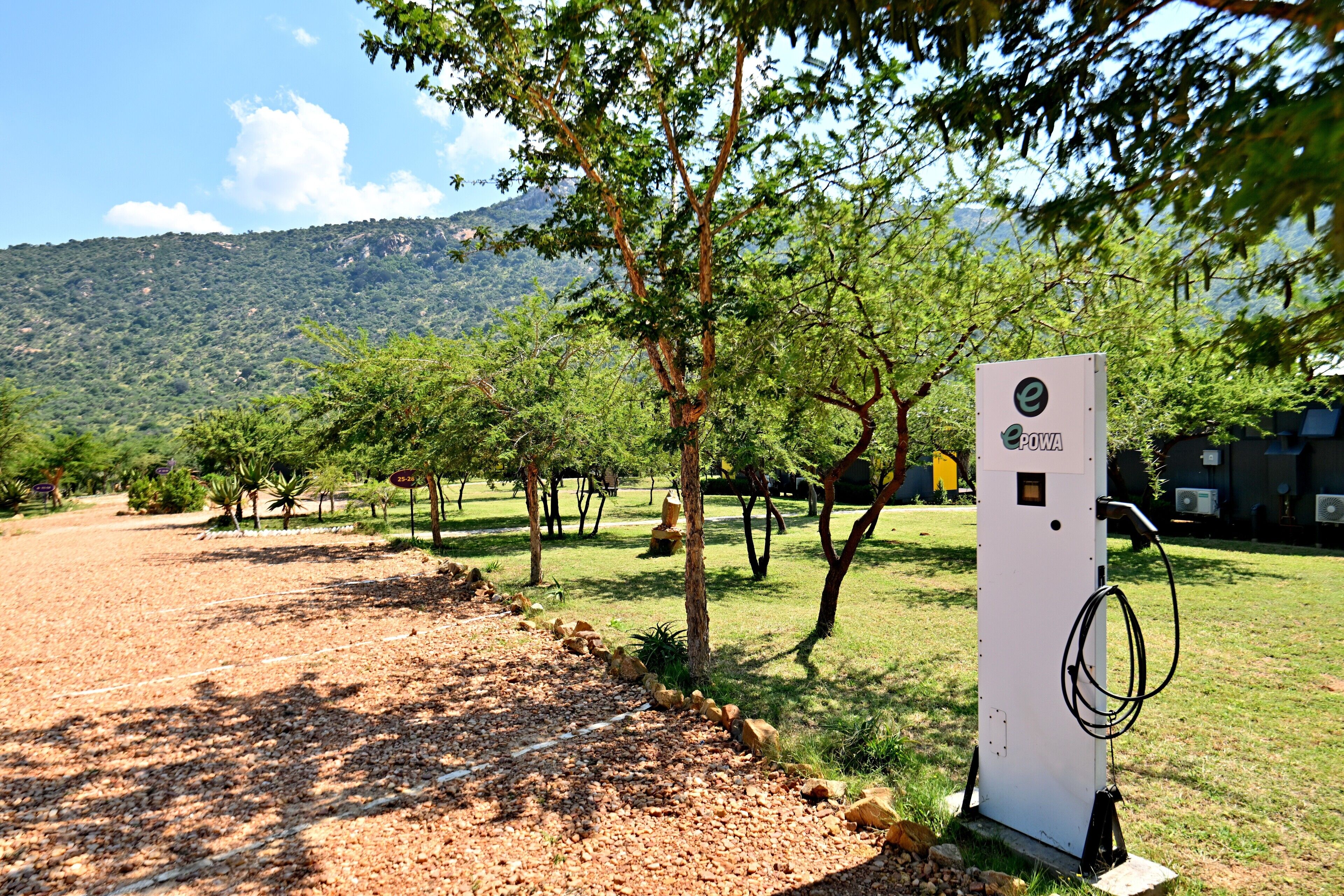 A solar-powered charging station in a park with trees and a mountain in the background.