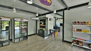 A modern interior with a 'Welcome' sign, refrigerated beverage dispensers, a seating area, and shelves stocked with snacks.