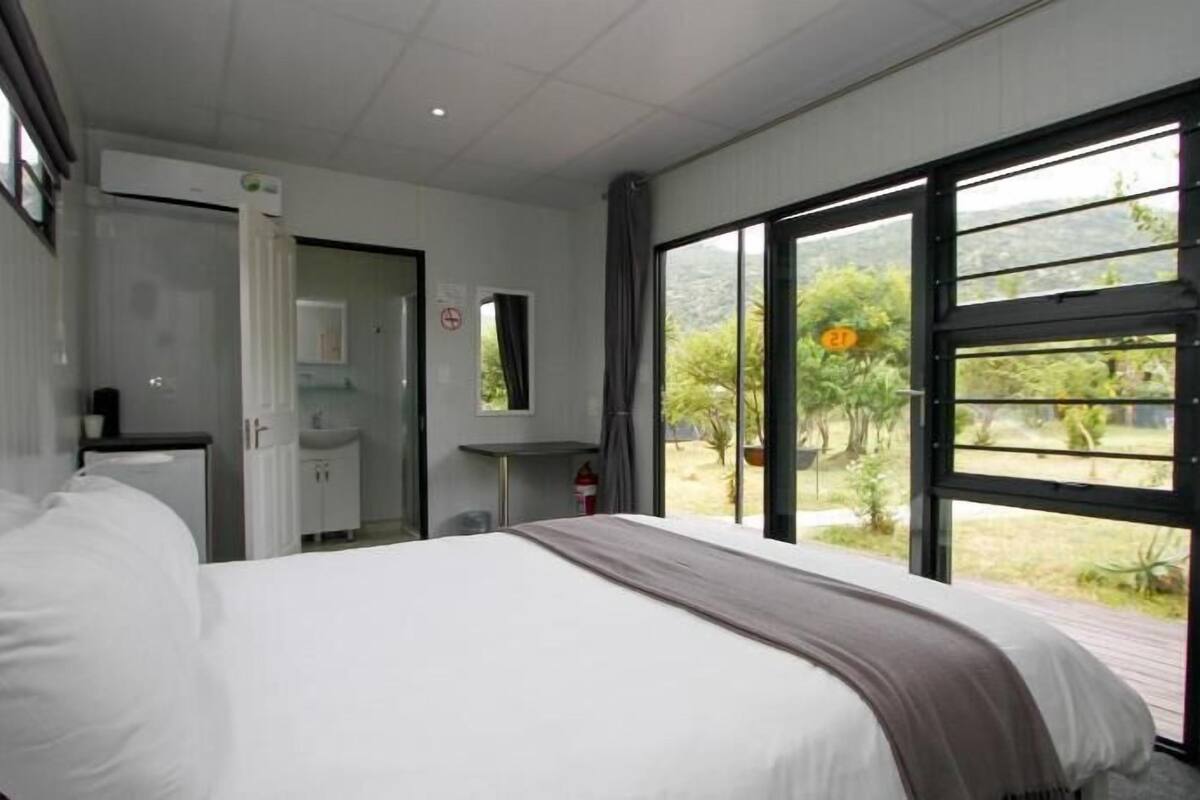 Un dormitorio con cama, baño y un ventanal con vistas a la vegetación.