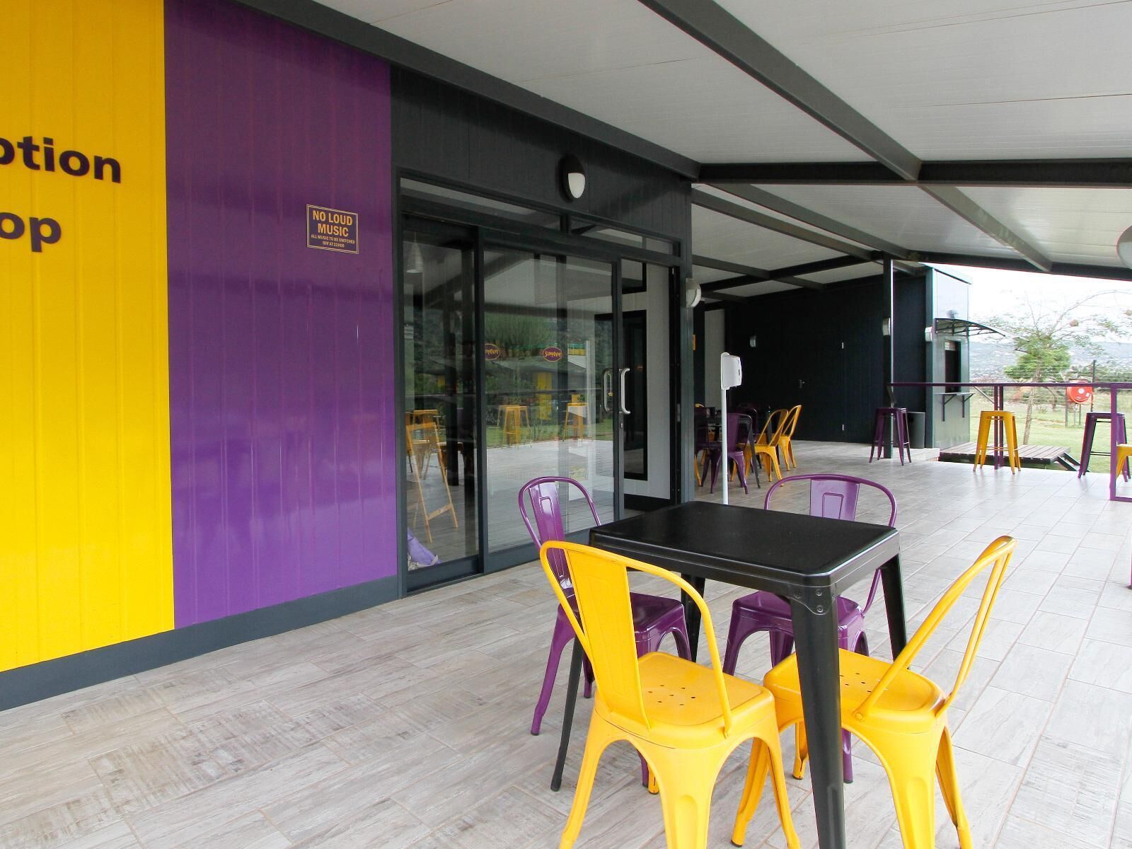 An outdoor seating area with yellow and purple chairs, a black table, and a glass door entrance.
