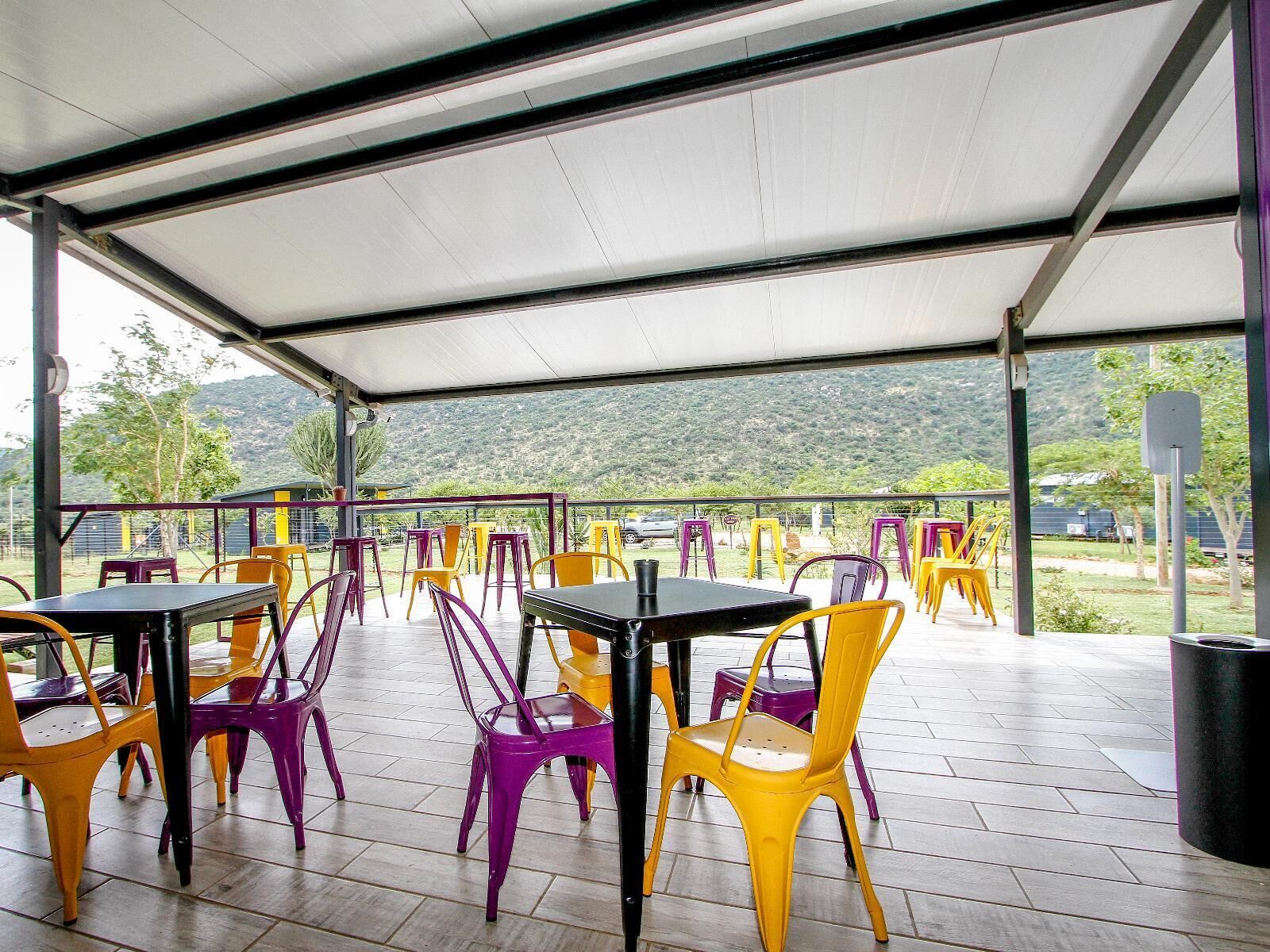 Un'area patio esterna con tavoli e sedie, un tetto coperto e vista su un paesaggio collinare.