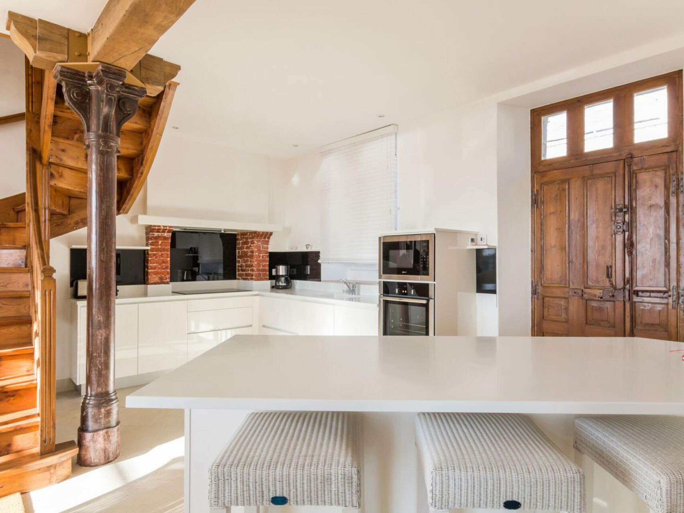 Una cocina moderna con armarios blancos, una escalera de madera y una puerta grande de madera.