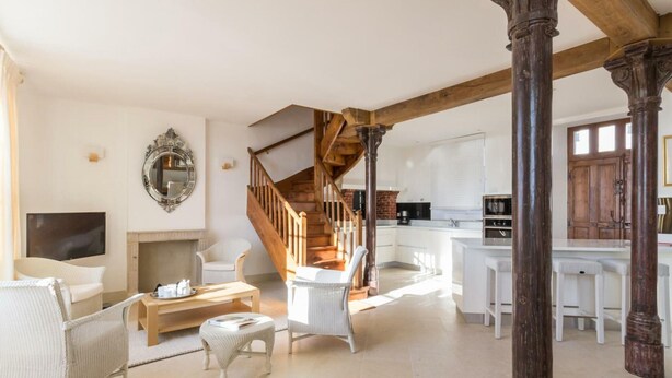 Een ruime woonkamer met een open haard, een houten trap en een keuken met witte kasten.