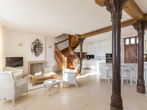 Amplia sala de estar con chimenea, una escalera de madera y una cocina con armarios blancos.