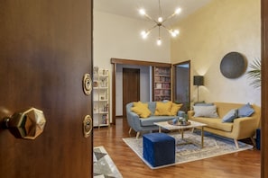 Un salon comprenant un canapé, une table basse et un pouf, une bibliothèque et une porte dotée d’une poignée en laiton.