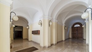 Un pasillo con techos abovedados, iluminación en la pared, una puerta de madera al final y suelo de mármol.