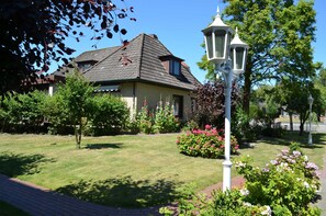 A house with a sloped roof, surrounded by a well-maintained garden with various plants and flowers. - A 3 GH 1-Room (TMS)(BC.n5) - Stranddomicil Steiner - Guesthouses (Büsum)