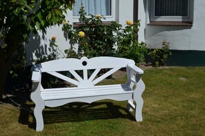 A white bench in a garden with a white building in the background. - A 3 GH 1-Room (TMS)(BC.n5) - Stranddomicil Steiner - Guesthouses (Büsum)
