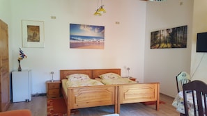 A bedroom with a wooden bed, a nightstand, a lamp, a small table with a vase of flowers, and two wall-mounted paintings.