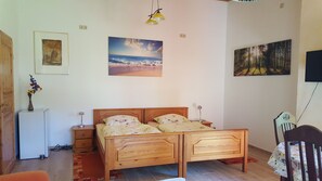 Un dormitorio con una cama de madera, una mesita de noche, una lámpara, una pequeña mesa con un florero y dos cuadros colgados en la pared.