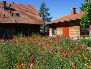 Una casa de madera con techo de tejas y un jardín lleno de flores rojas.