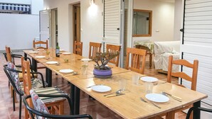 A dining area with a long wooden table set for four, surrounded by wooden chairs. There is a potted plant on the table, and a sofa is visible in the background. - 6 bedroom beautiful home in La Azohia (La Azohia)