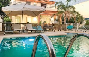 Une piscine entourée d’une clôture en bois et de palmiers, avec des chaises longues et des parasols.