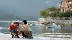 A waterfront scene with a stone wall, boats, and a building with balconies. - Stunning home in Rabac (Rabac)
