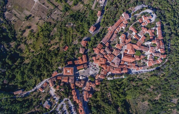 Une vue aérienne d’une ville avec une place centrale, entourée de bâtiments aux toits recouverts de tuiles rouges, et de vastes espaces verts.