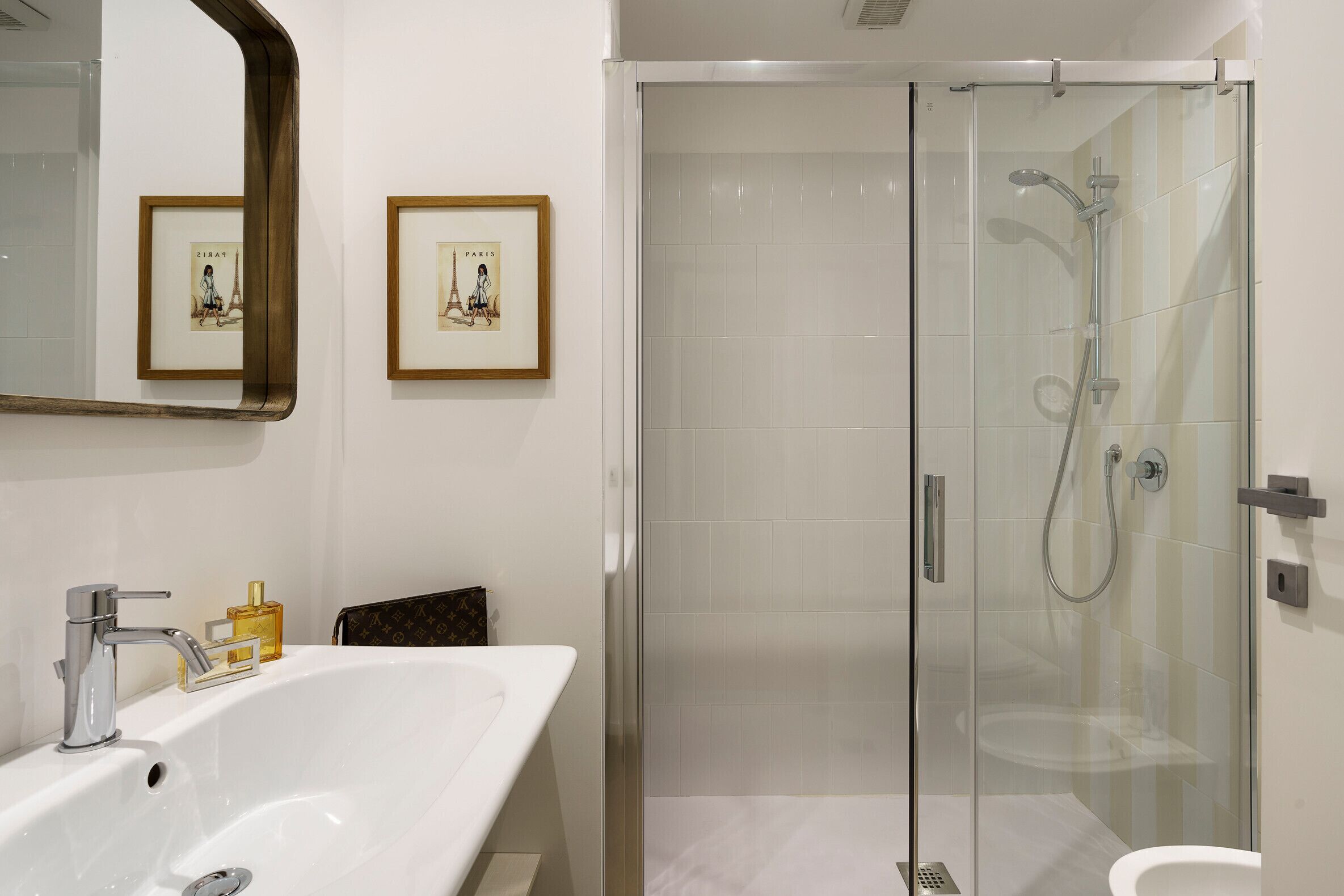 Ein modernes Badezimmer mit einer gläsernen Duschkabine, einem großen weißen Waschbecken und gerahmten Bildern an der Wand.