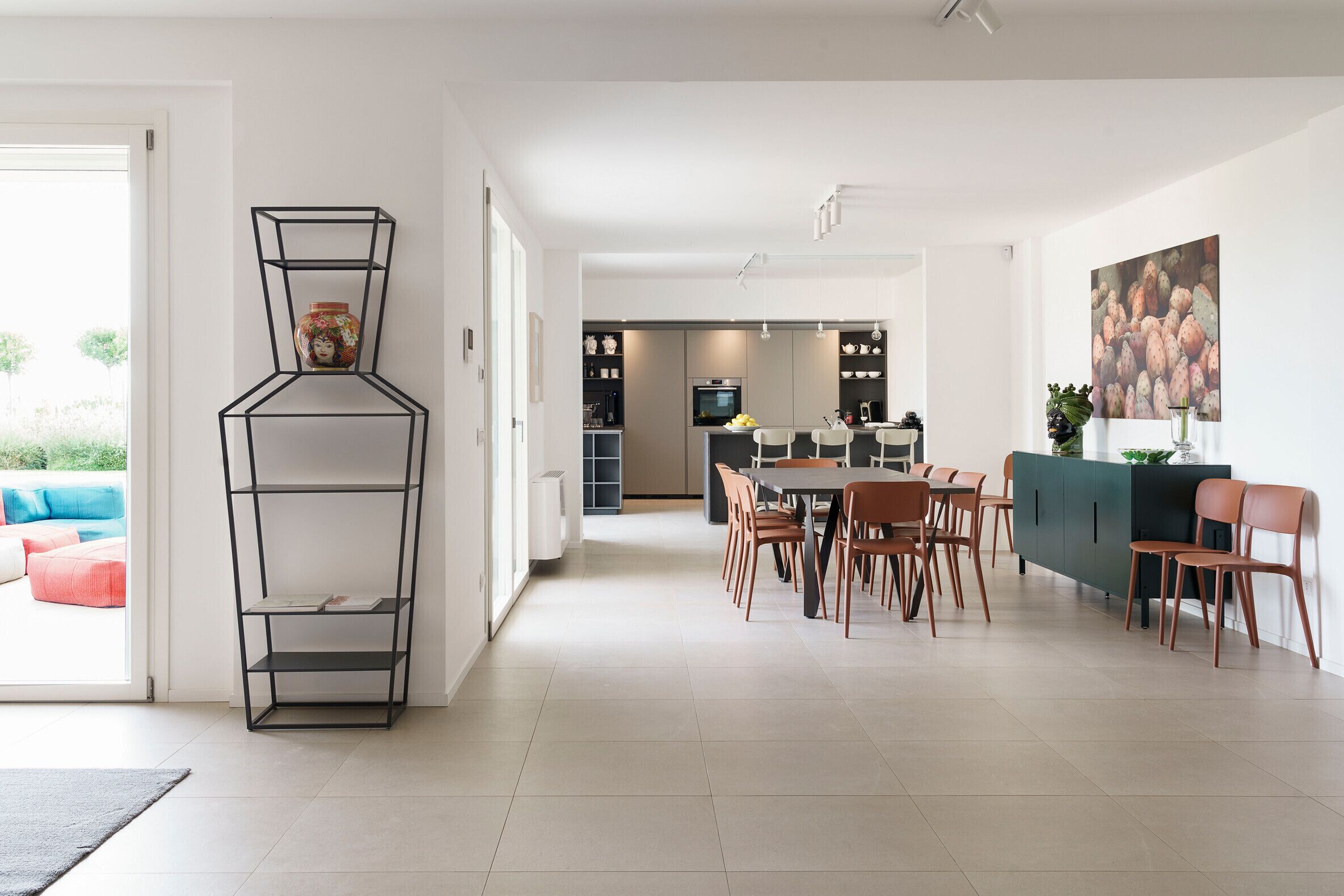 A modern kitchen with a dining area, featuring a geometric shelving unit, a dining table with chairs, and a kitchen island with a sink and appliances.