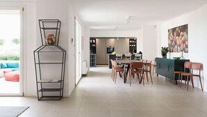 Eine moderne Küche mit Essbereich, ausgestattet mit einem geometrischen Regalsystem, einem Esstisch mit Stühlen und einer Kücheninsel mit Spüle und Geräten.