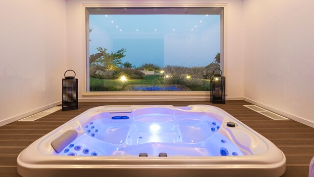 Ein Whirlpool in einem Raum mit großem Fenster, Holzboden und zwei schwarzen Laternen.