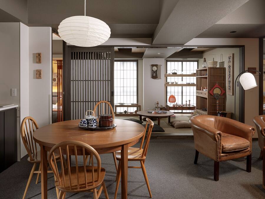 A modern living room with a dining area, featuring a wooden dining table, leather chairs, and a traditional Japanese sliding door.