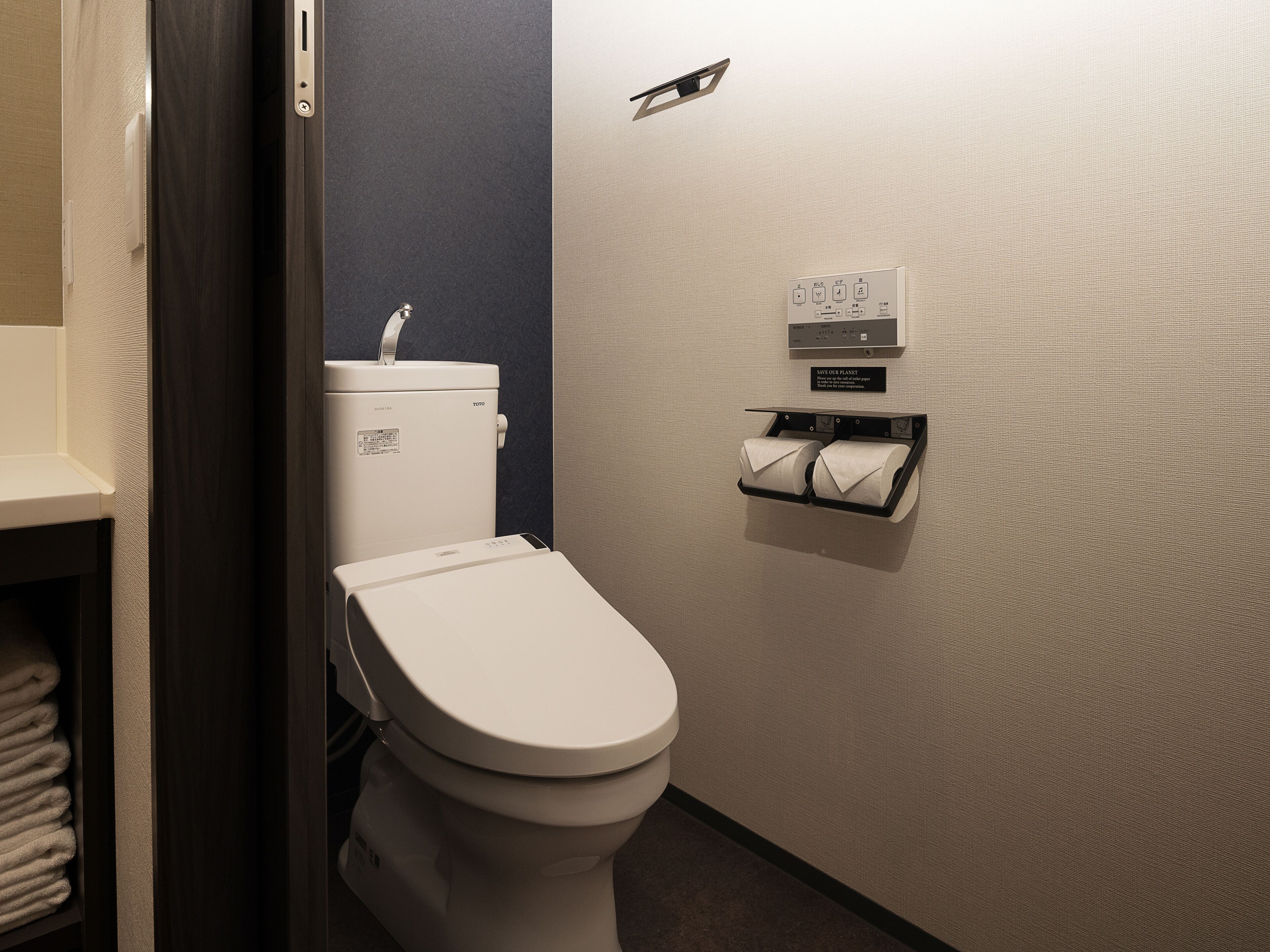 Uma casa de banho moderna com sanita, porta-toalhas e dispensador de papel higiénico fixado na parede.