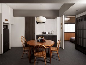 Een moderne eetruimte met een ronde houten tafel, vier houten stoelen, een hanglamp en een keuken op de achtergrond.