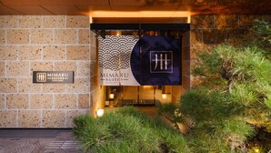 The exterior of Mimaru Suites in Kyoto Central, featuring a stone facade, signage, and a well-lit entrance with surrounding greenery. - MIMARU SUITES Kyoto Central (Kyoto)