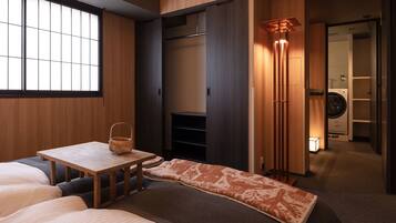 A hotel room with a bed, a small table with a basket, a wardrobe, and a washing machine in the background.