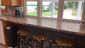 Una cocina con encimeras de granito, cafetera y vistas a un lago a través de amplios ventanales.