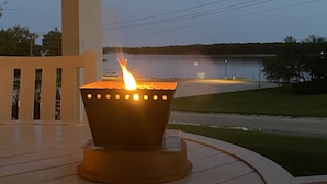Una mesa con una vela encendida en un soporte metálico, con vista a un cuerpo de agua y un área cubierta de césped.
