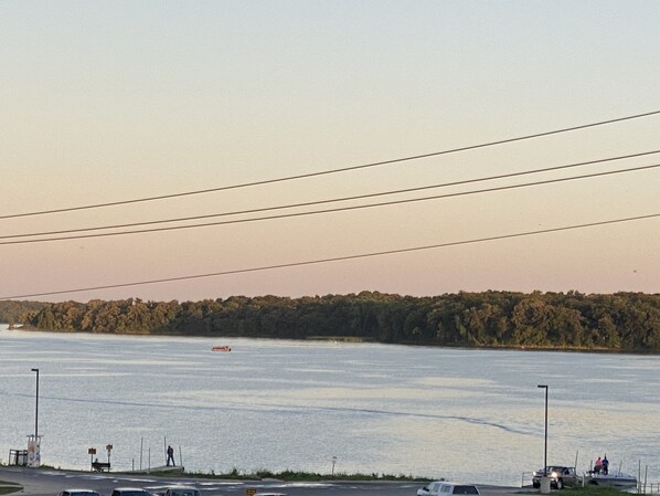 Blick auf das Wasser mit einer Straße, einem Boot und einem bewaldeten Gebiet in der Ferne.