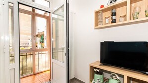 Ein Zimmer mit einer Schiebeglastür, die auf einen Balkon führt, einem Fernseher auf einer Holzablage und einem Heizkörper an der Wand.