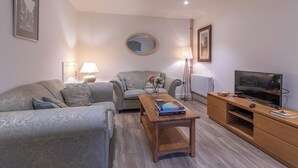 A living room with a sofa, a coffee table, a TV, and a lamp. - Plum Guide - Acting Sweet (York)