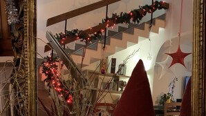 Une pièce avec un grand miroir qui reflète un sapin de Noël décoré, une figurine de gnome et un escalier orné de guirlandes festives.