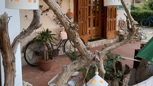 Un espace extérieur rustique agrémenté d’une branche d’arbre décorée de lanternes suspendues, d’une porte en bois et d’un vélo en arrière-plan.