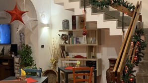 Un salon moderne avec un escalier décoré de guirlandes de Noël, un coin repas avec une table et des chaises, et un téléviseur placé à gauche.