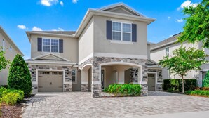 A two-story residential building with a stone facade, a garage, and a paved driveway. - Spectacular Home near Disney: Waterpark, Theater, Pool Table - 332SF (Kissimmee)