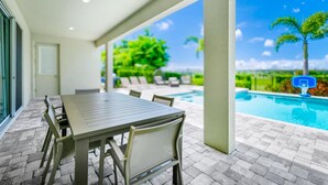 An outdoor patio with a table and chairs, a pool, and a view of palm trees. - Spectacular Home near Disney: Waterpark, Theater, Pool Table - 332SF (Kissimmee)