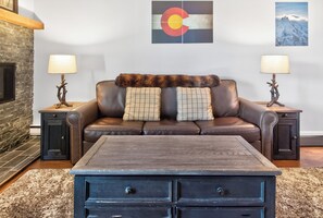 A living room with a brown leather sofa, two side tables with lamps, a fireplace, and a wall with two framed pictures. - Ski In - Ski Out. Perfect Location. Hot Tub. Pool. (Breckenridge)