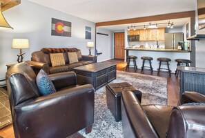 A modern living room with leather furniture, a coffee table, and a kitchen area with wooden cabinets and bar stools. - Ski In - Ski Out. Perfect Location. Hot Tub. Pool. (Breckenridge)